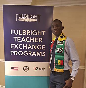 Lamine Cisse standing beside a banner for Fulbright Teacher Exchanges
