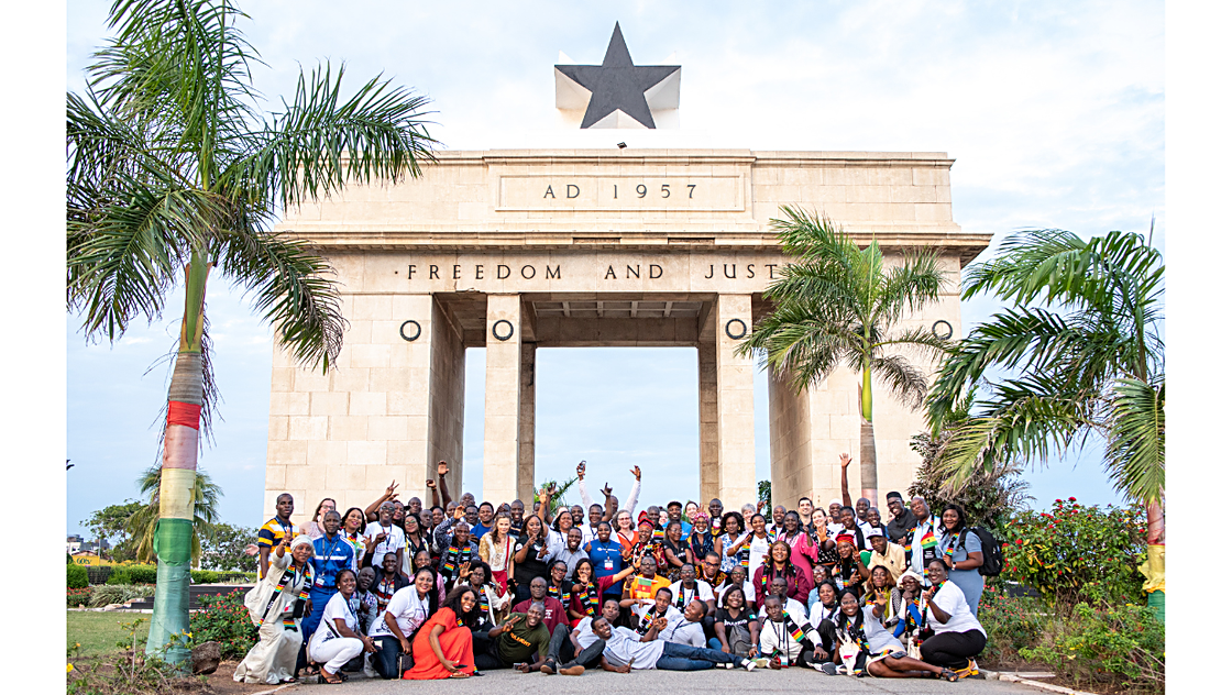 A group of people posed under the Black Star Gate in Accra, reading FREEDOM AND JUSTICE
