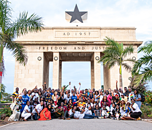 A group of people posed under the Black Star Gate in Accra, reading FREEDOM AND JUSTICE