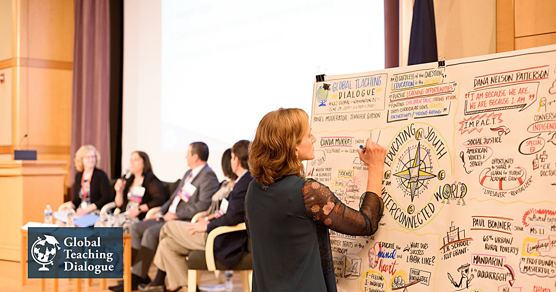 woman draws on a whiteboard at a panel during the Global Teaching Dialogue.