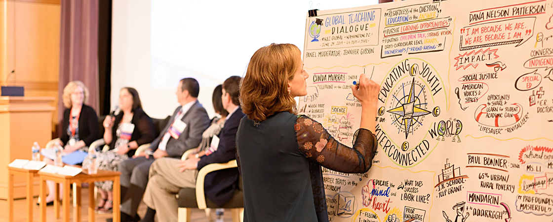 woman draws on a whiteboard at a panel during the Global Teaching Dialogue.
